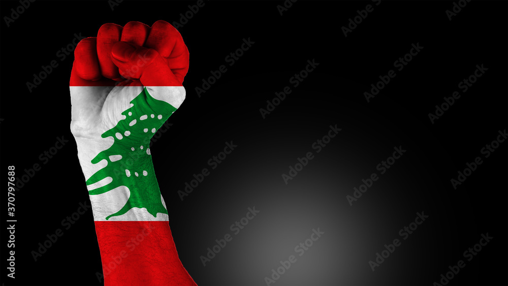 Concept of an uprising and political turmoil in Lebanon. Low key picture of a fist painted in colors of the Lebanese flag on a black background.