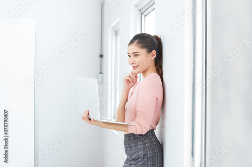 young businesswoman standing in front of window and working on laptop computer