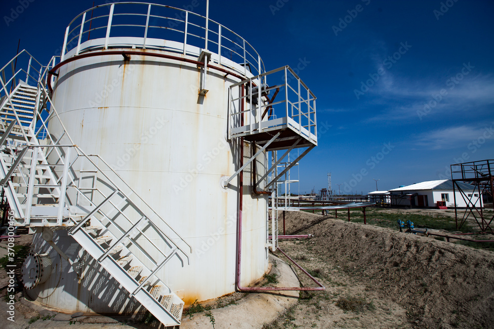 White oil storage tank under bright sun on  deep blue sky with light clouds. Oil refinery (oil processing) plant in desert. Near Taraz city, Kazakhstan.