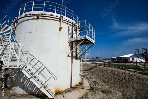 White oil storage tank under bright sun on  deep blue sky with light clouds. Oil refinery (oil processing) plant in desert. Near Taraz city, Kazakhstan.