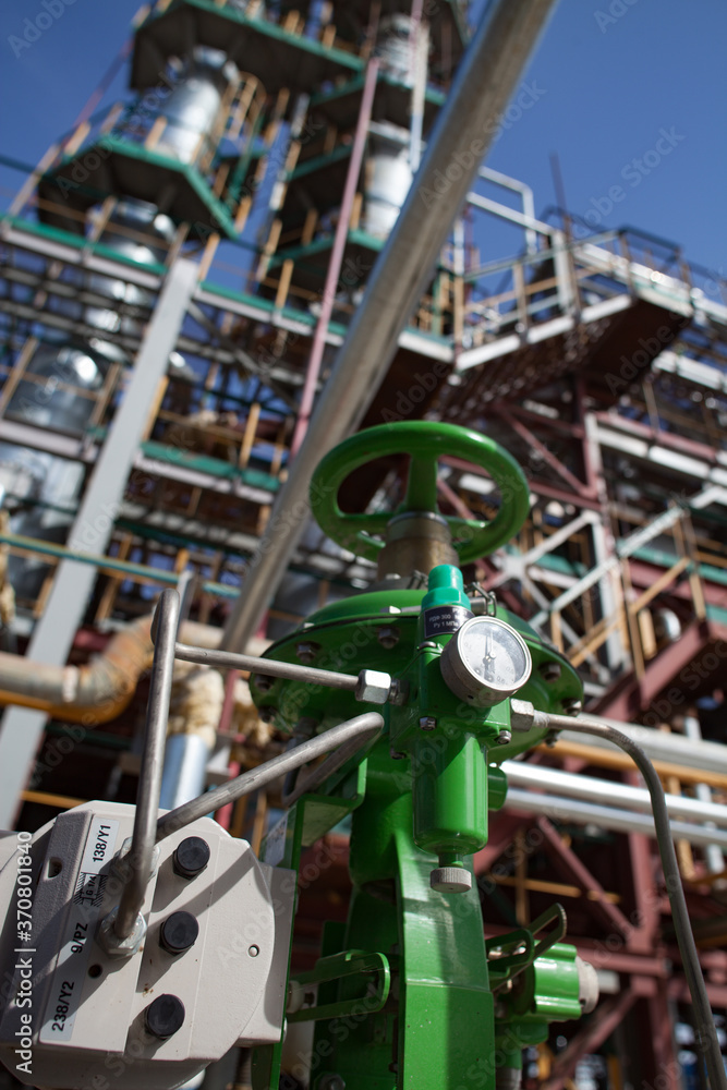Fototapeta premium Green pressure measuring device (gauge) at the oil processing plant. Grey oil refining columns (distillation tower), pipelines on background. Deep blue sky. Near Taraz city. Kazakhstan
