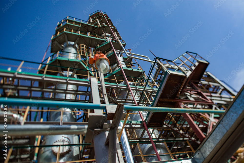Grey oil distillation towers (refining columns) and pipelines at the oil refinery plant on blue sky background. Taraz city. Kazakhstan. Grey oil distillation towers (refining columns) and pipelines at the oil refinery plant on blue sky background. Taraz city. Kazakhstan.