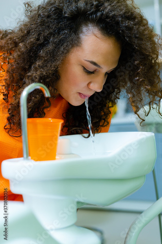 Teenage girl rinse mouth after treatment at dental office, spitting water in cuspidor - ceramic bowl