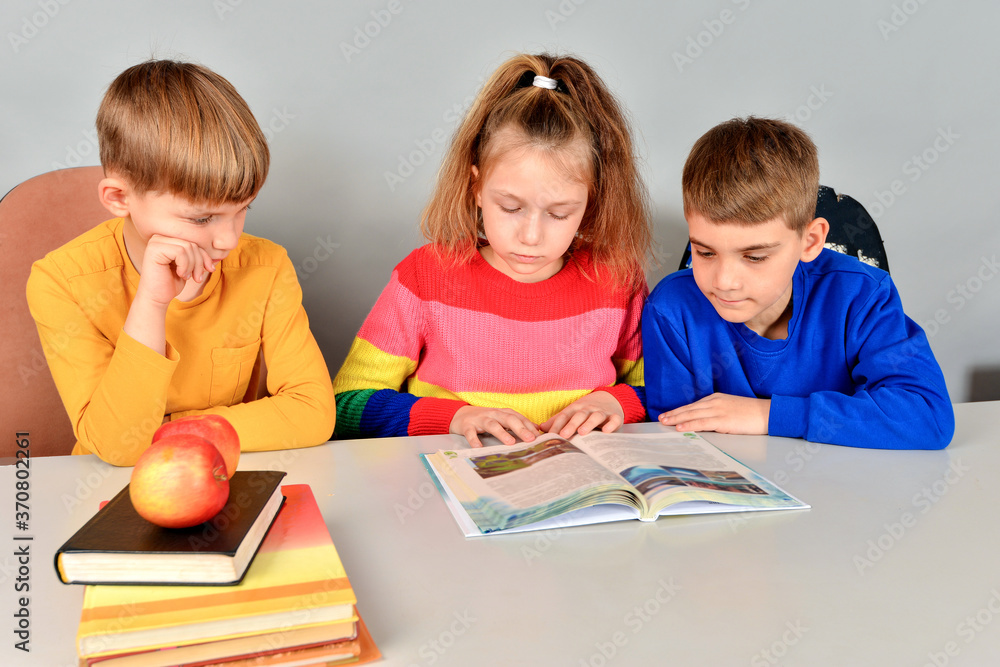 Two brothers and sister are reading a book on a white table. Two brothers and sister are reading a book on a white table.