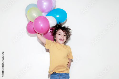 niño de 5 a 7 años brincando con una sonrisa mientras sostiene globos de colores sobre un fondo blanco 