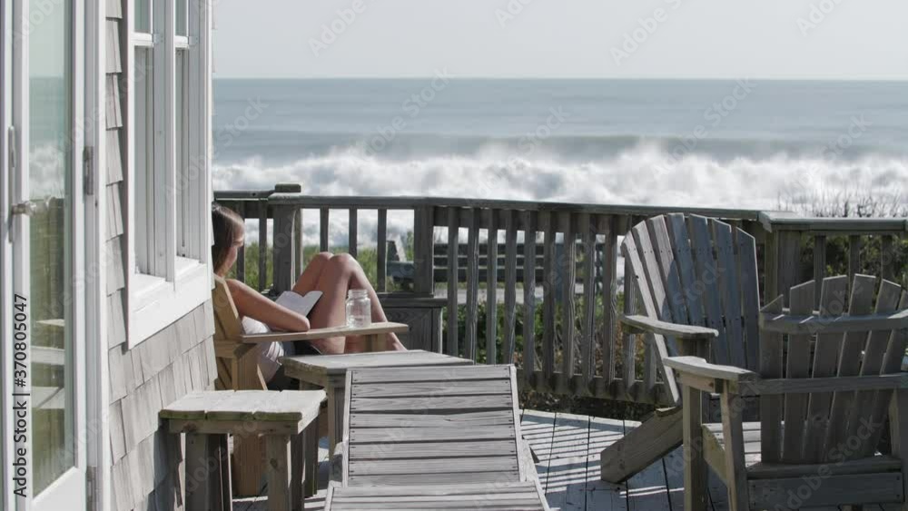 Girl reading on sun deck by the beach with large waves breaking Girl reading on sun deck by the beach with large waves breaking