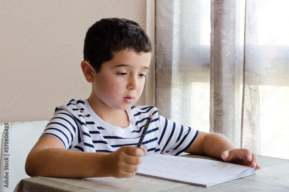Niño con camiseta de rayas estudiando en casa Niño con camiseta de rayas estudiando en casa