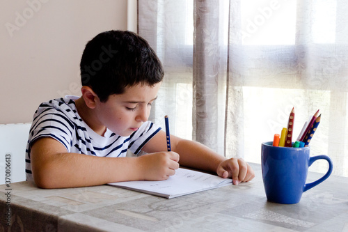 Niño con camiseta de rayas concentrado y escribiendo mientras aprende en casa photo