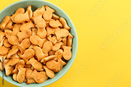 Delicious goldfish crackers in bowl on yellow background, top view. Space for text