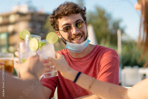 A guy and his riends having a celebrative toast. Schoolmates reunion after the coronavirus pandemic quarantine lockdown. People drinking mojito cocktails outdoors. photo