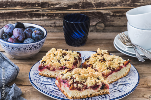 Tableau sur toile Three pieces of plum cake with crumble on a bluewhite plate on a wooden table