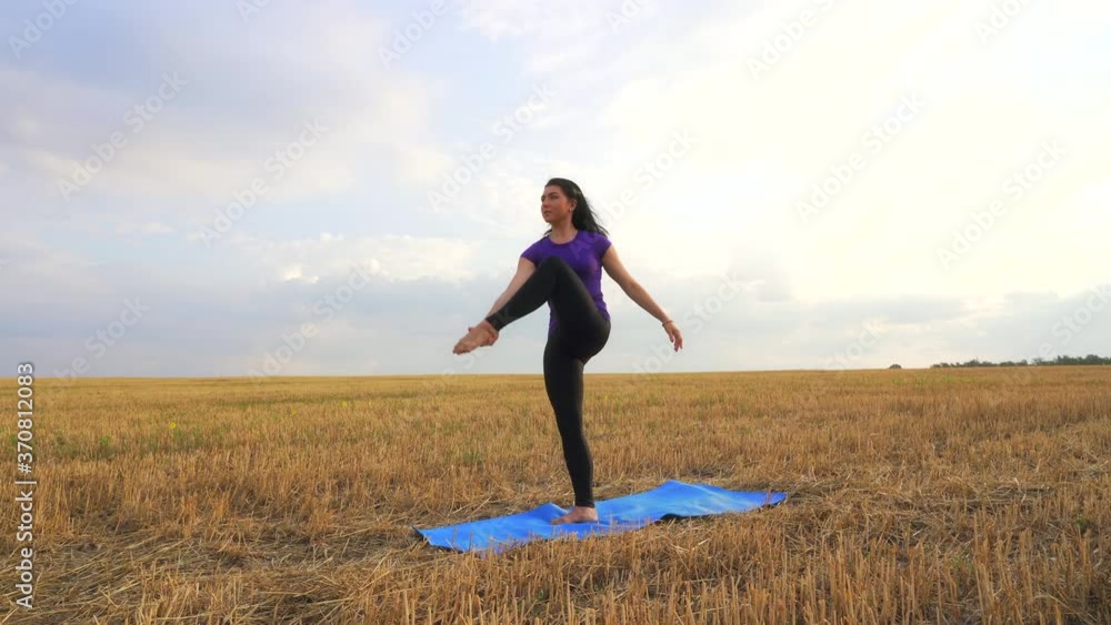 Young woman is practicing yoga outdoor at dawn. Stretching exercise on field with nature view, flexible body. Sport, fitness, health care, wellness and lifestyle concept. Young woman is practicing yoga outdoor at dawn. Stretching exercise on field with nature view, flexible body. Sport, fitness, health care, wellness and lifestyle concept.