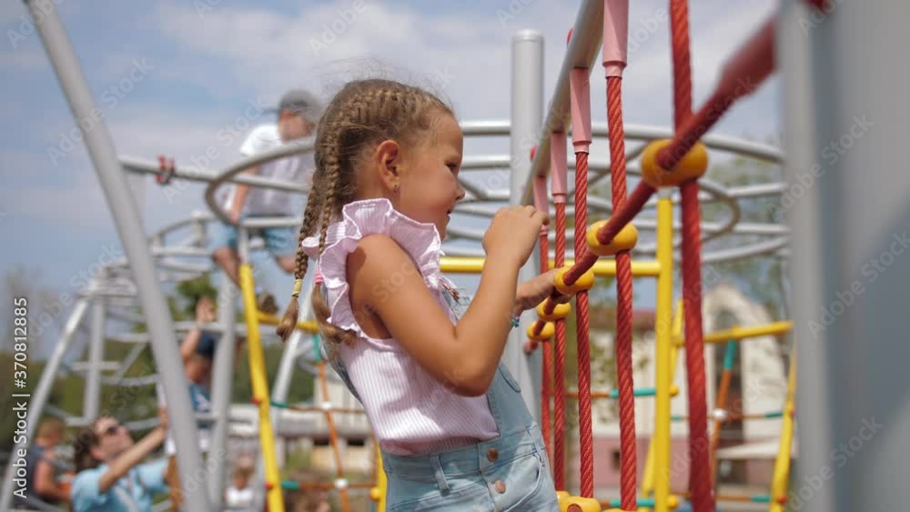 Little girl climbs up rope wall on playground Little girl climbs up rope wall on playground