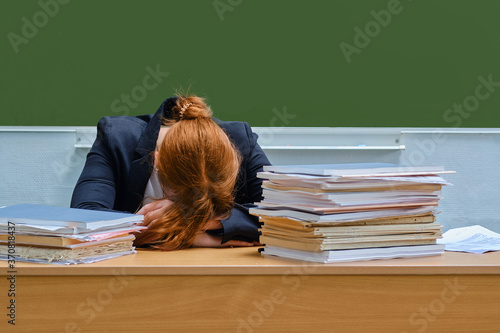 Fotografie Woman teacher sleeps resting her head at school desk, copy space