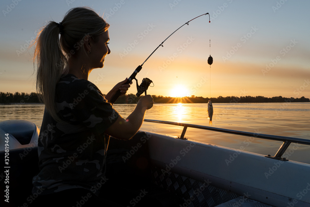 Obraz premium A woman on a fishing trip caught a fish.Fishing on the lake from a boat. Fishing rods in sunlight. Fishing rest concept. 
