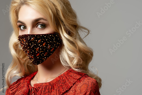 Woman wearing stylish dark red velvet protective face mask with golden rhinestones, beads. Fashion accessory during quarantine of coronavirus. Close up studio portrait. Copy, empty space for text