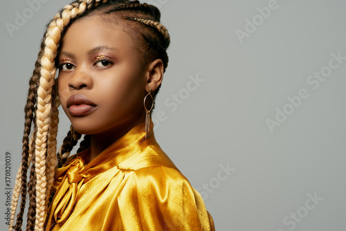 Close up beauty portrait of young attractive African American woman with many braids hairstyle, wearing trendy yellow silk blouse. Copy, empty space for text photo