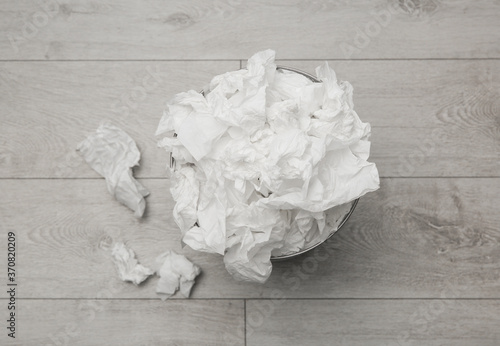 Used paper tissues and trash can on wooden floor, flat lay photo