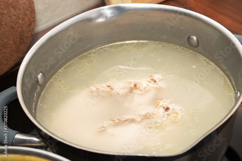 A healthy wholesome chicken breast broth is cooked on a stove in a saucepan