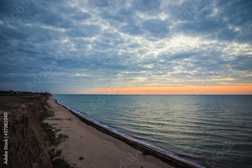 Predawn sky at the sea on a cloudy morning. Ships can be seen against the background of sunrise on the horizon. Dropping off the sandy coastline. Black sea. Sanzhiika. Ukraine