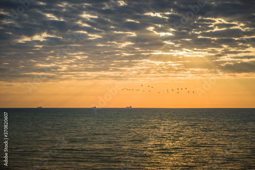 Golden sunrise at the sea on a cloudy morning. Ships can be seen against the background of sunrise on the horizon. A flock of birds against the sky. Black sea. Sanzhiika. Ukraine © decorator