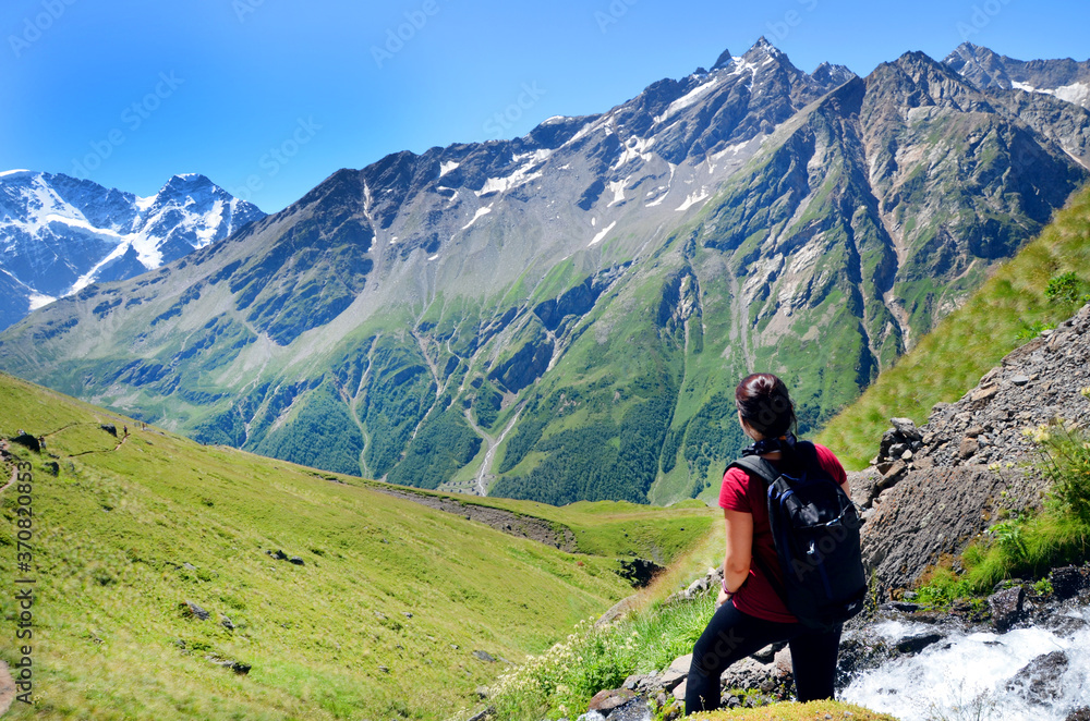 Tourist standing back over beautiful view on caucasian mountains and blue sky in summer. Nature of the Elbrus region.