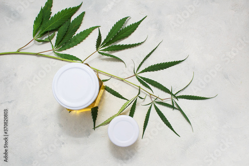 Hemp oil bottlse lies with green hemp leaves on white wooden background. Alternative medicine