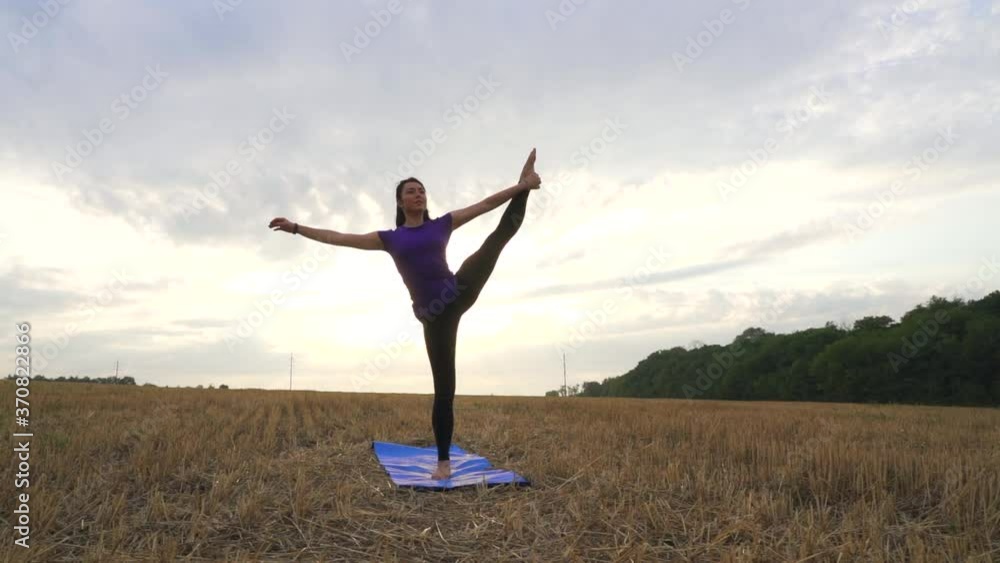 Young woman is practicing yoga outdoor on the grass at dawn. Stretching exercise on field with nature view, flexible body. Sport, fitness, health care, wellness and lifestyle concept. Young woman is practicing yoga outdoor on the grass at dawn. Stretching exercise on field with nature view, flexible body. Sport, fitness, health care, wellness and lifestyle concept.