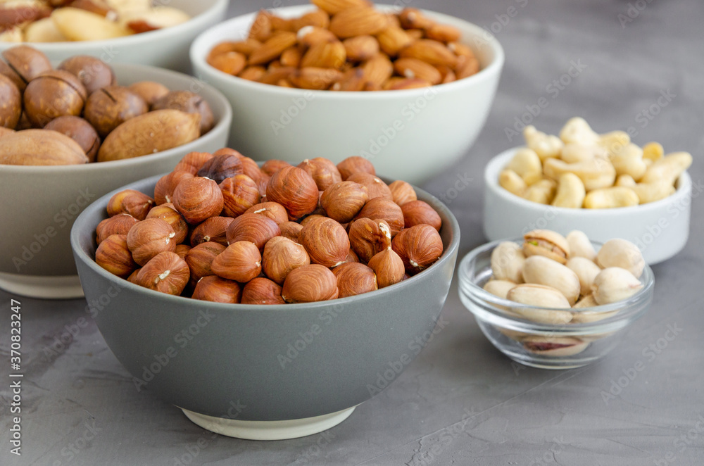 Hazelnuts, almonds, Brazilian nuts, cashews, macadamia, pecans and pistachios in bowls on a dark concrete background. Healthy food. Horizontal, copy space. Hazelnuts, almonds, Brazilian nuts, cashews, macadamia, pecans and pistachios in bowls on a dark concrete background. Healthy food. Horizontal, copy space.