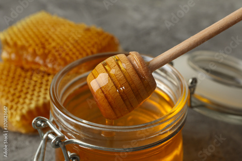 Honeycombs and glass jar with honey on gray background