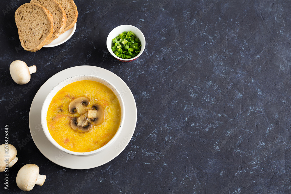 Champignon soup in a white bowl. Whole champignons, bread and cut green onions on a blue background. Top of the soup is decorated with slices of sliced mushroom. Top view, place for text composition Champignon soup in a white bowl. Whole champignons, bread and cut green onions on a blue background. Top of the soup is decorated with slices of sliced mushroom. Top view, place for text composition