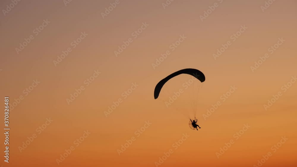 dark silhouette of Moto Paraglider flies, soars in the air, against the background of a bright orange sunset dark silhouette of Moto Paraglider flies, soars in the air, against the background of a bright orange sunset