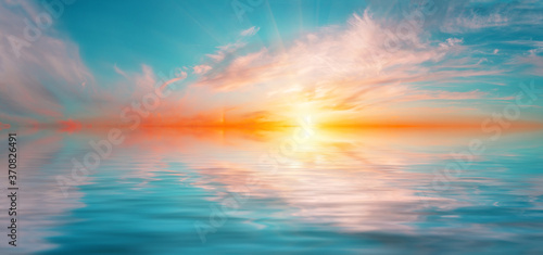 Panorama of morning dramatic sky with bright sun above water surface © alexlukin