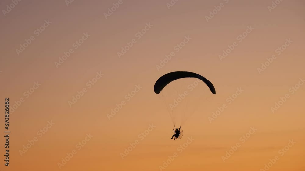 dark silhouette of Moto Paraglider flies, soars in the air, against the background of a bright orange sunset dark silhouette of Moto Paraglider flies, soars in the air, against the background of a bright orange sunset