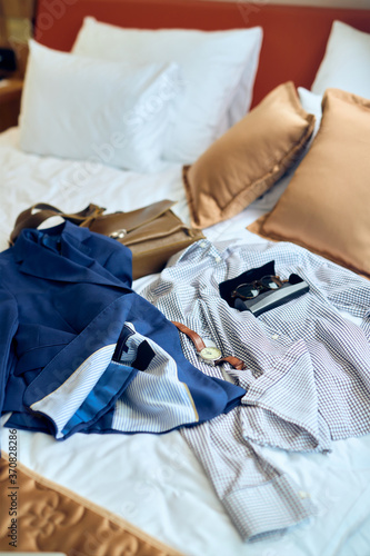 Men's accessorises and businesswear on a bed in hotel room.