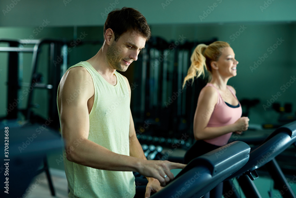 Smiling athlete adjusting speed on a treadmill in a gym. Smiling athlete adjusting speed on a treadmill in a gym.