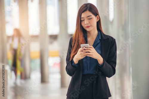 Asian Thai girl using mobile phone in business market.Person front view of Young Woman holding smartphone via internet to sending message and searching on digital device.Technology Concept.