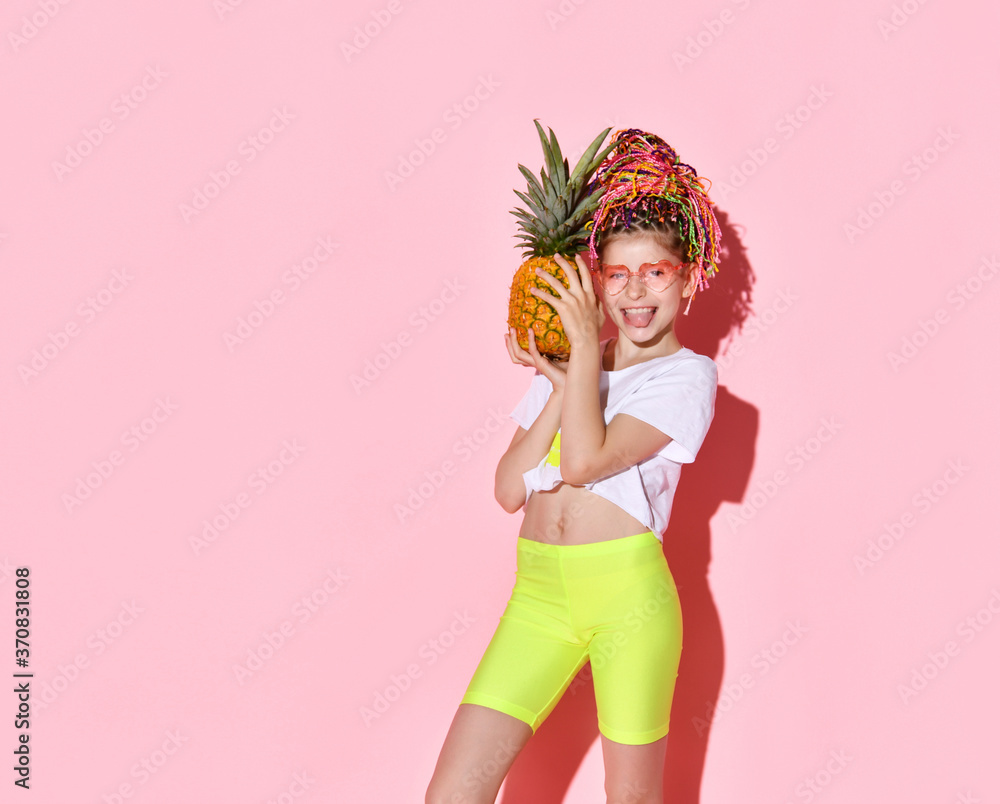 Teenage female with african pigtails, in sunglasses. She is holding pineapple and smiling, posing on pink background. Close up Teenage female with african pigtails, in sunglasses. She is holding pineapple and smiling, posing on pink background. Close up