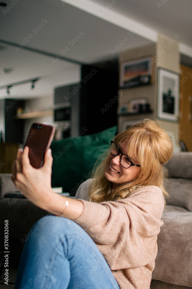 Content female sitting on floor on soft carpet and taking photo on mobile phone while drinking hot beverage in a mug relaxing at home Content female sitting on floor on soft carpet and taking photo on mobile phone while drinking hot beverage in a mug relaxing at home