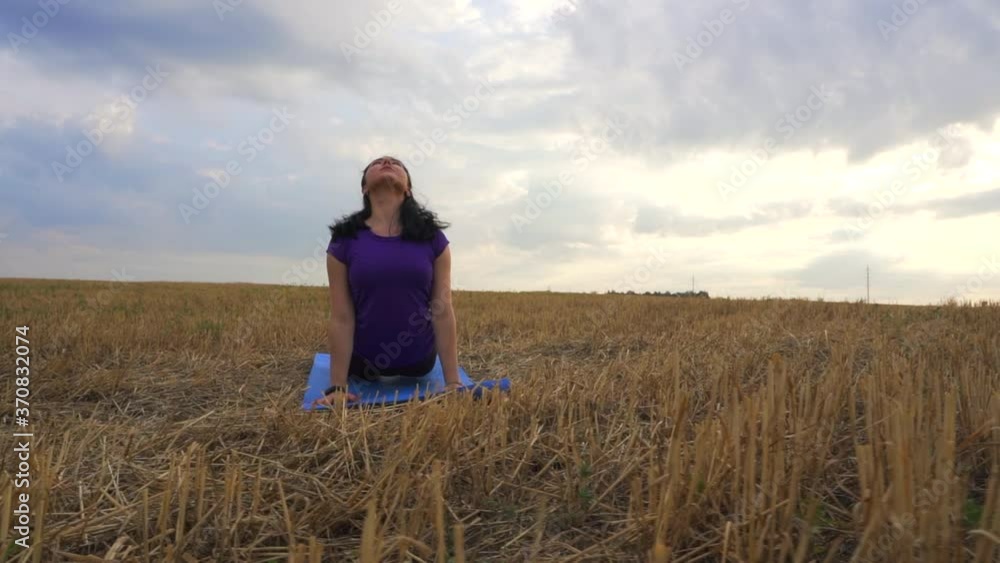 Young woman is practicing yoga outdoor on the grass at dawn. Stretching exercise on field with nature view, flexible body. Sport, fitness, health care, wellness and lifestyle concept. Young woman is practicing yoga outdoor on the grass at dawn. Stretching exercise on field with nature view, flexible body. Sport, fitness, health care, wellness and lifestyle concept.