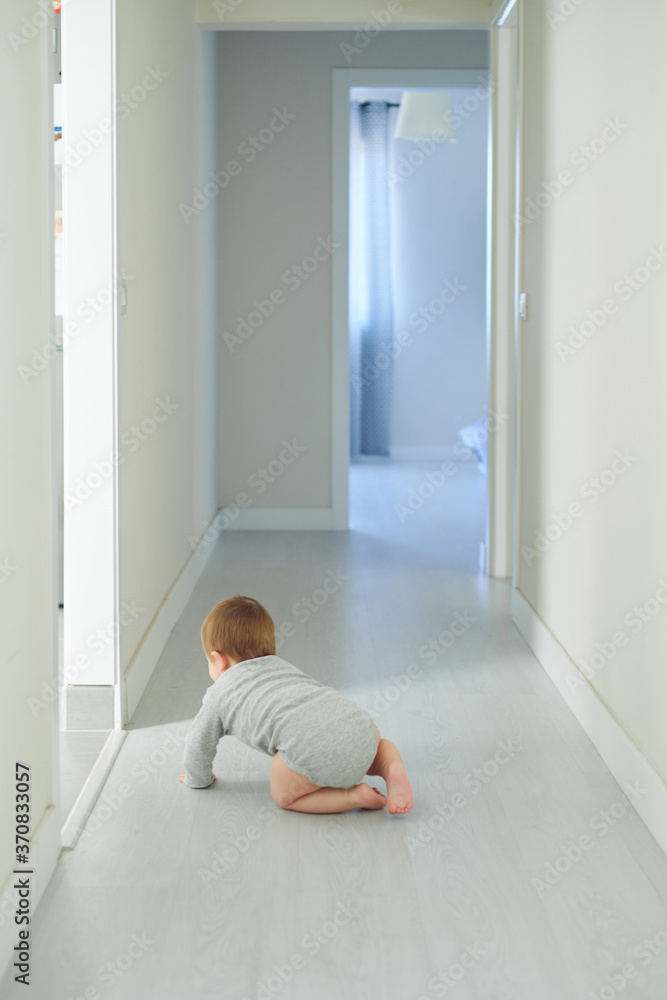 Back view of anonymous little baby in gray bodysuit crawling on floor in cozy room at home Back view of anonymous little baby in gray bodysuit crawling on floor in cozy room at home