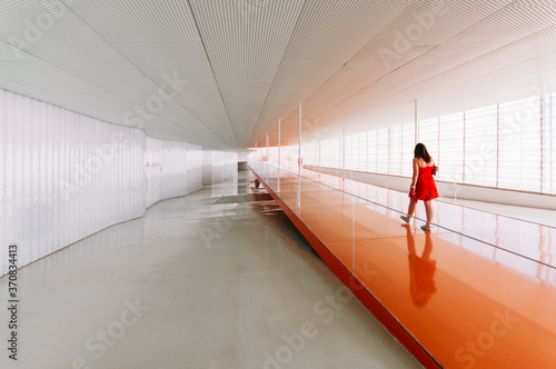 Back view of unrecognizable female standing on shiny orange floor of passage in modern building photo