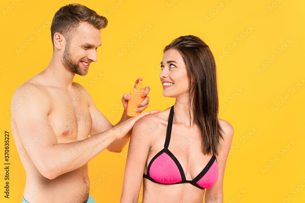  man smiling while applying sunblock on cheerful woman isolated on yellow