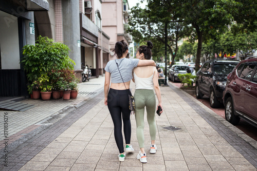 Happy slim young Asian female in casual clothes embracing friends shoulder while walking together along busy street in Taipei photo