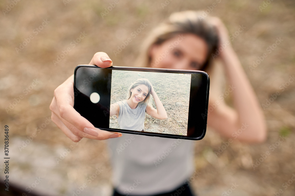 High angle of playful young female making face and showing tongue while taking selfie on smartphone in summer day on street High angle of playful young female making face and showing tongue while taking selfie on smartphone in summer day on street