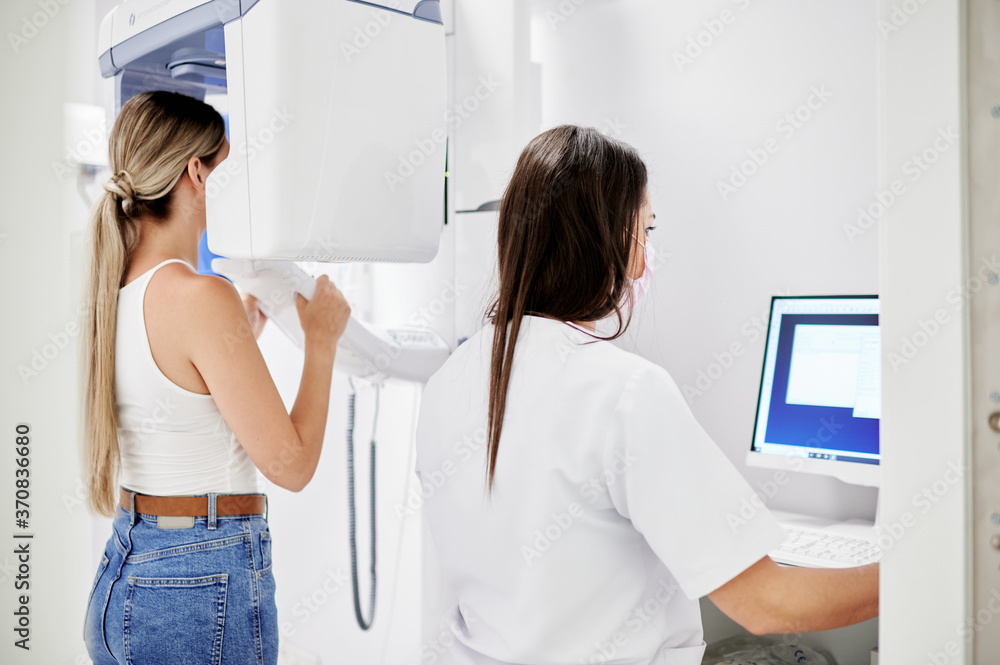 Back view of female dentist using computer while making X ray scan to blond woman in contemporary dental clinic Back view of female dentist using computer while making X ray scan to blond woman in contemporary dental clinic