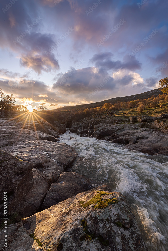 Picturesque scenery of rapid creek flowing through rough stony terrain under colorful cloudy sunset sky Picturesque scenery of rapid creek flowing through rough stony terrain under colorful cloudy sunset sky