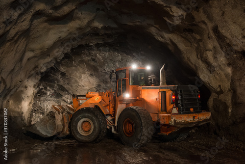 Modern excavator with illuminated headlights placed on dirty soil in underground mine during mining work photo