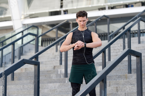 Relaxation exercises. Runner looking at wearable sports watch. checking pulse on watches. fit man checking time. Young Sporty Male With Fit Body In Sportswear Using Fitness Tracker