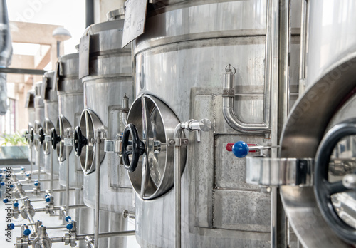 Identical big stainless steel cisterns with metal tubes and fixing pieces of silver color put in row